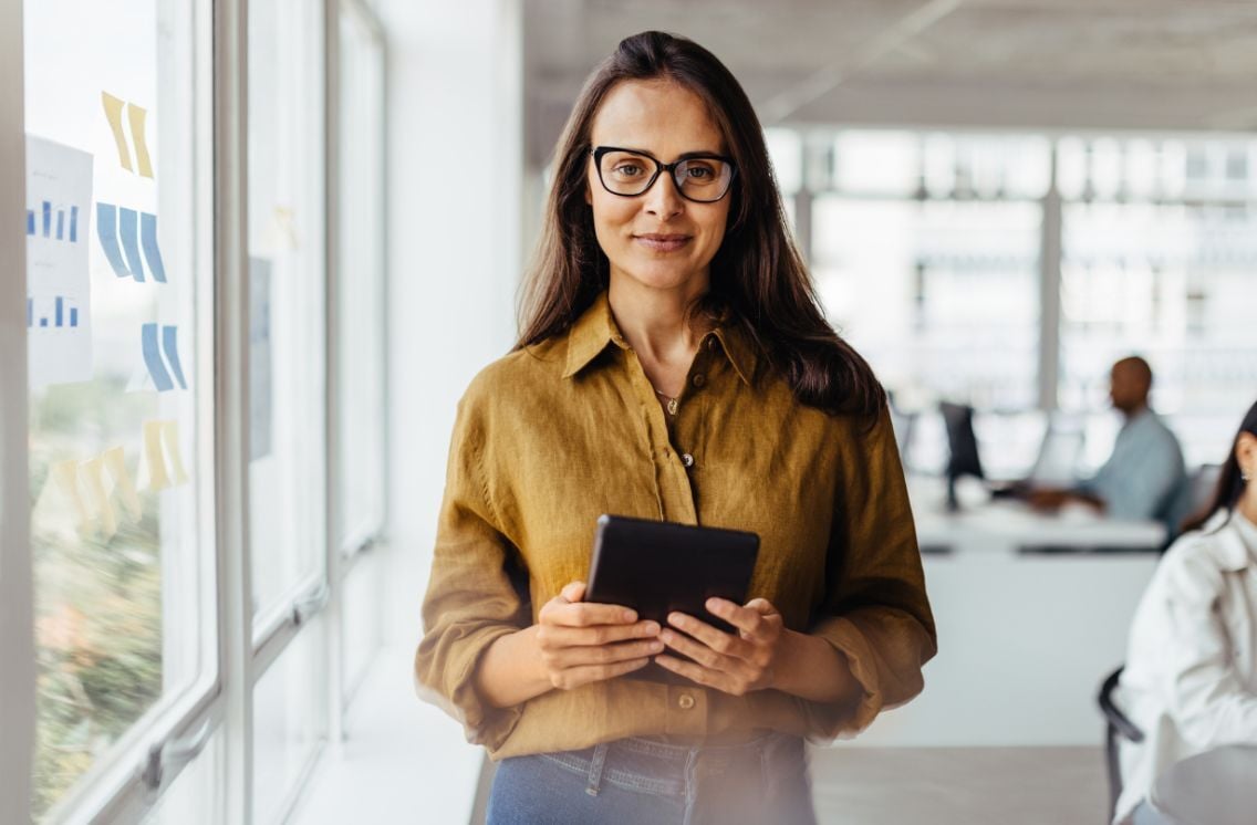 Confident professional woman holding a tablet in a modern office, representing the expertise of biotechnology executive recruiters in identifying leadership talent.