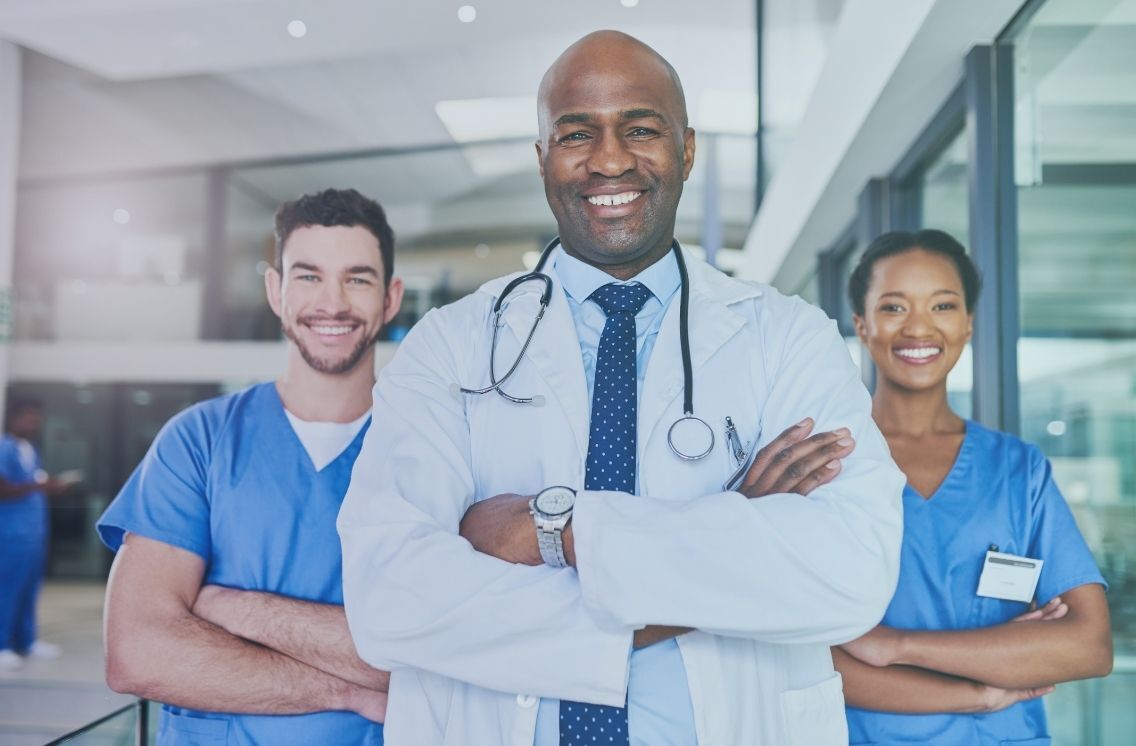Group of confident healthcare professionals in scrubs smiling in a hospital corridor, representing the impact of medical field recruiters on healthcare staffing success.