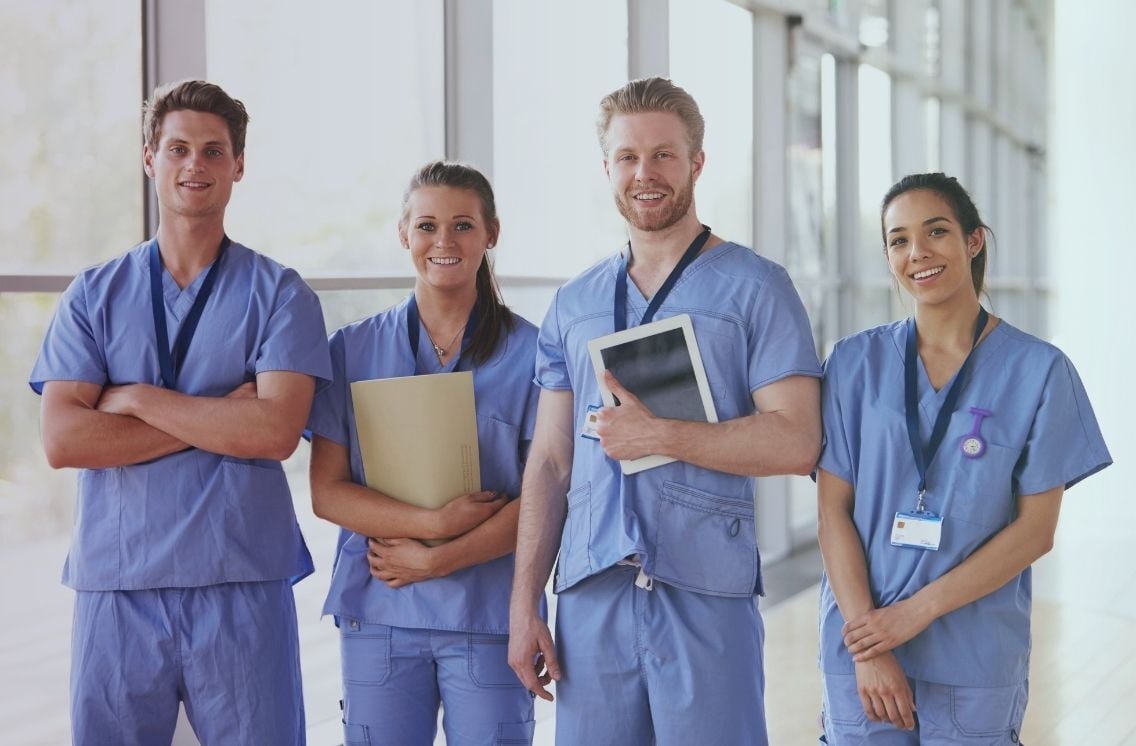 Four smiling healthcare professionals in scrubs standing in a hospital corridor, symbolizing effective healthcare recruiting and RPO solutions.