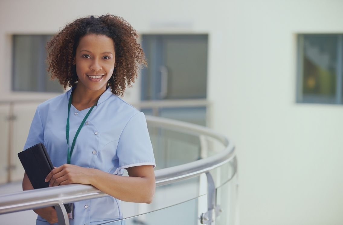 Smiling nurse standing in a healthcare facility, representing nursing recruitment agencies.